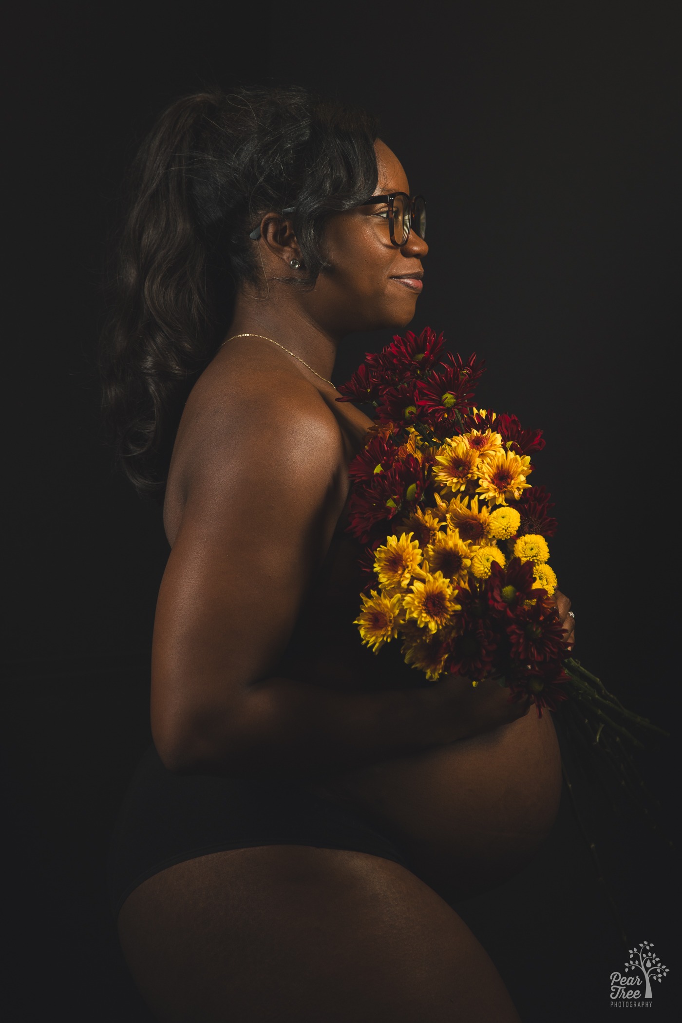 Smiling and pregnant mom holding flowers over her chest and belly for maternity photographs in Kennesaw