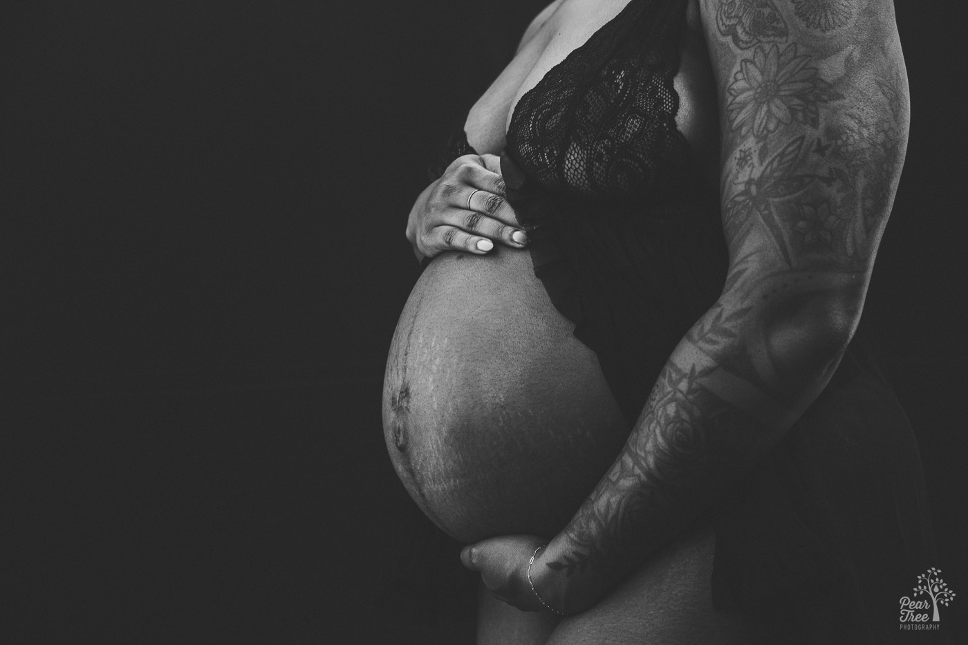 Black and white close up maternity photograph of a tattooed African American mom-to-be holding her belly