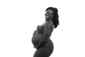 Black and white photograph of a pregnant momma with a long pony tail holding her belly and smiling