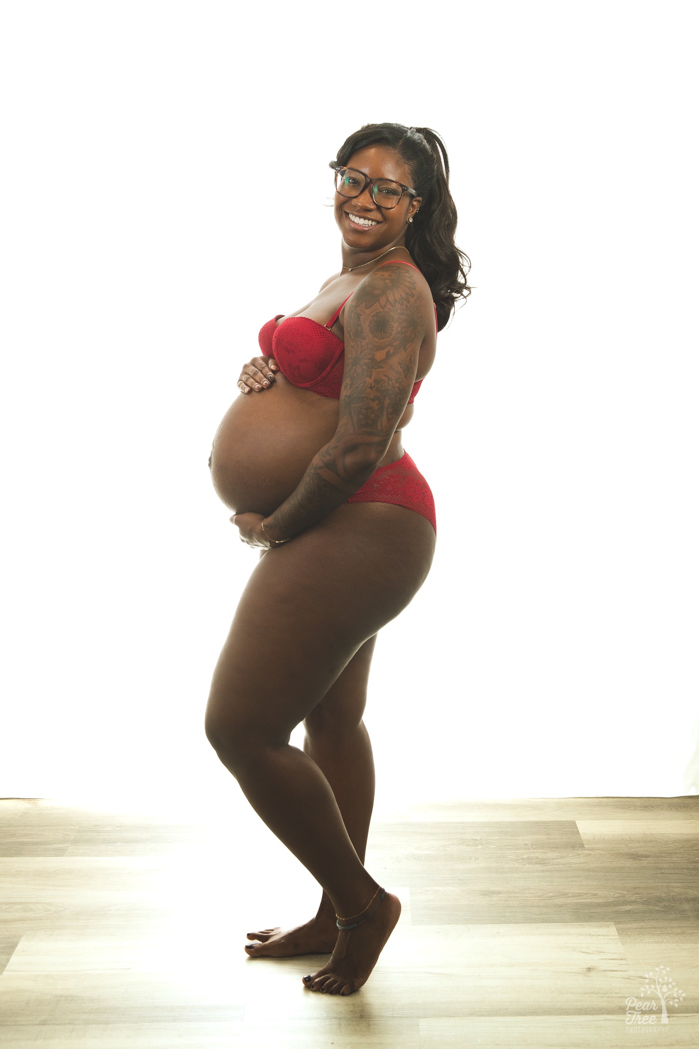 Kennesaw maternity photography session with a smiling African American woman wearing glasses and holding her pregnant belly