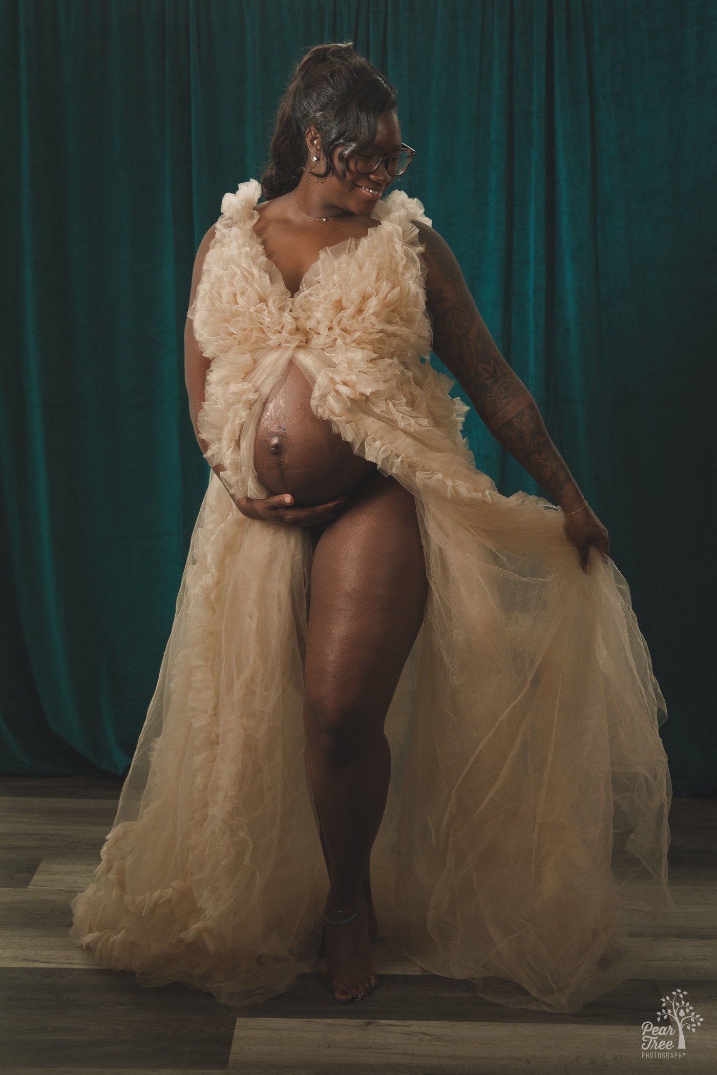 Pregnant and happy mom-to-be holding her pregnant belly while fluffing her ruffled chiffon dress in a Kennesaw photography studio