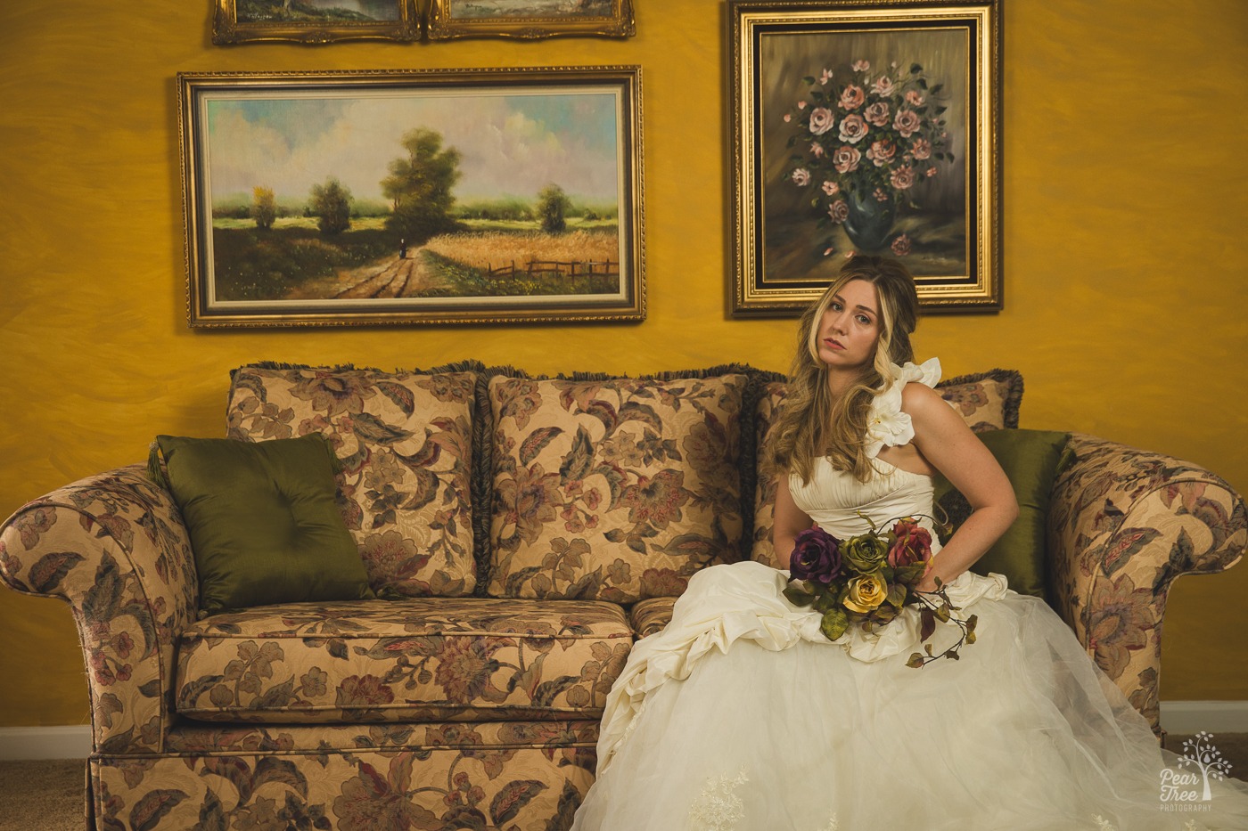 Alley Bei sitting on a sofa in her old wedding dress looking sad while holding her dried bouquet