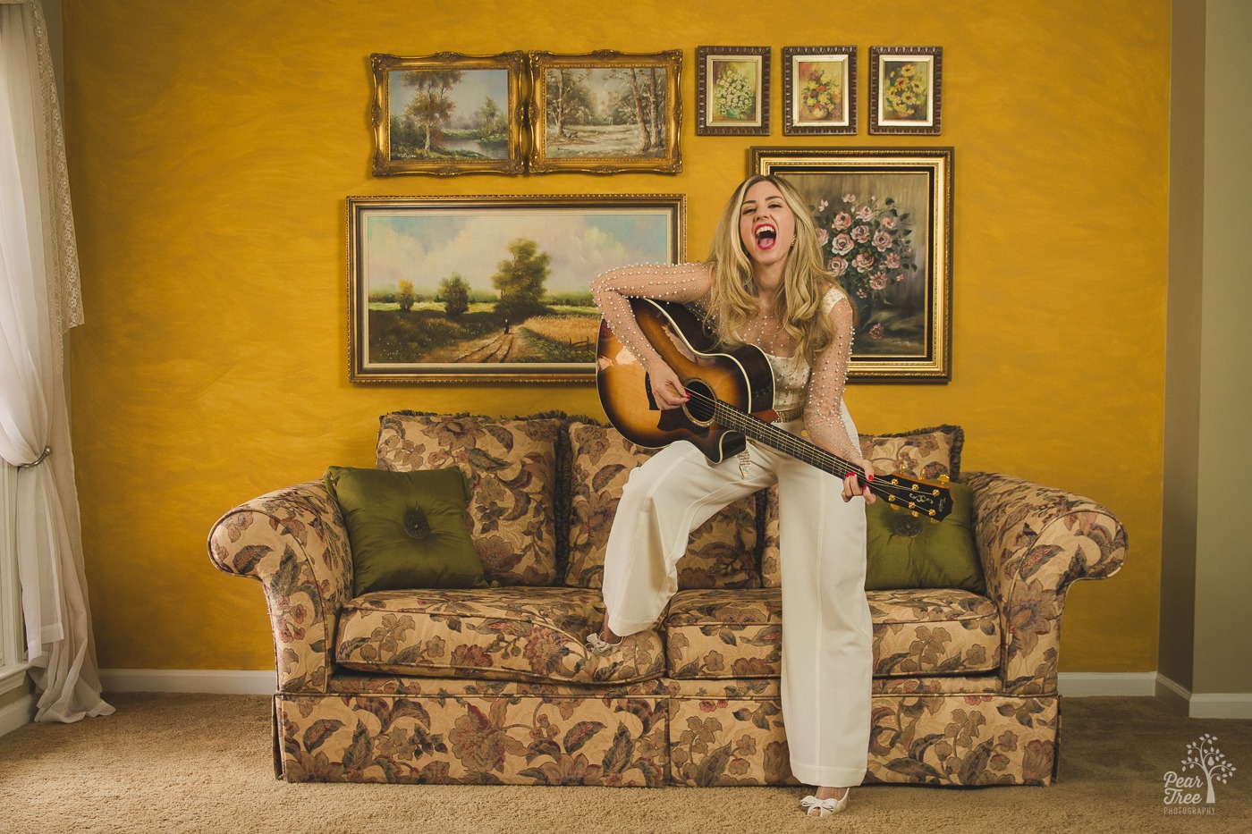 Alley Bei singing her heart out while playing the guitar with one foot on the floor and one on the sofa cushions