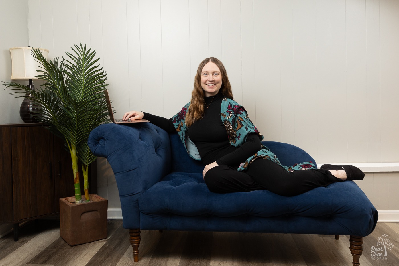 Dr. Hillary Langley sitting with her laptop on the edge of a chaise lounge and smiling for an East Cobb headshot photographer