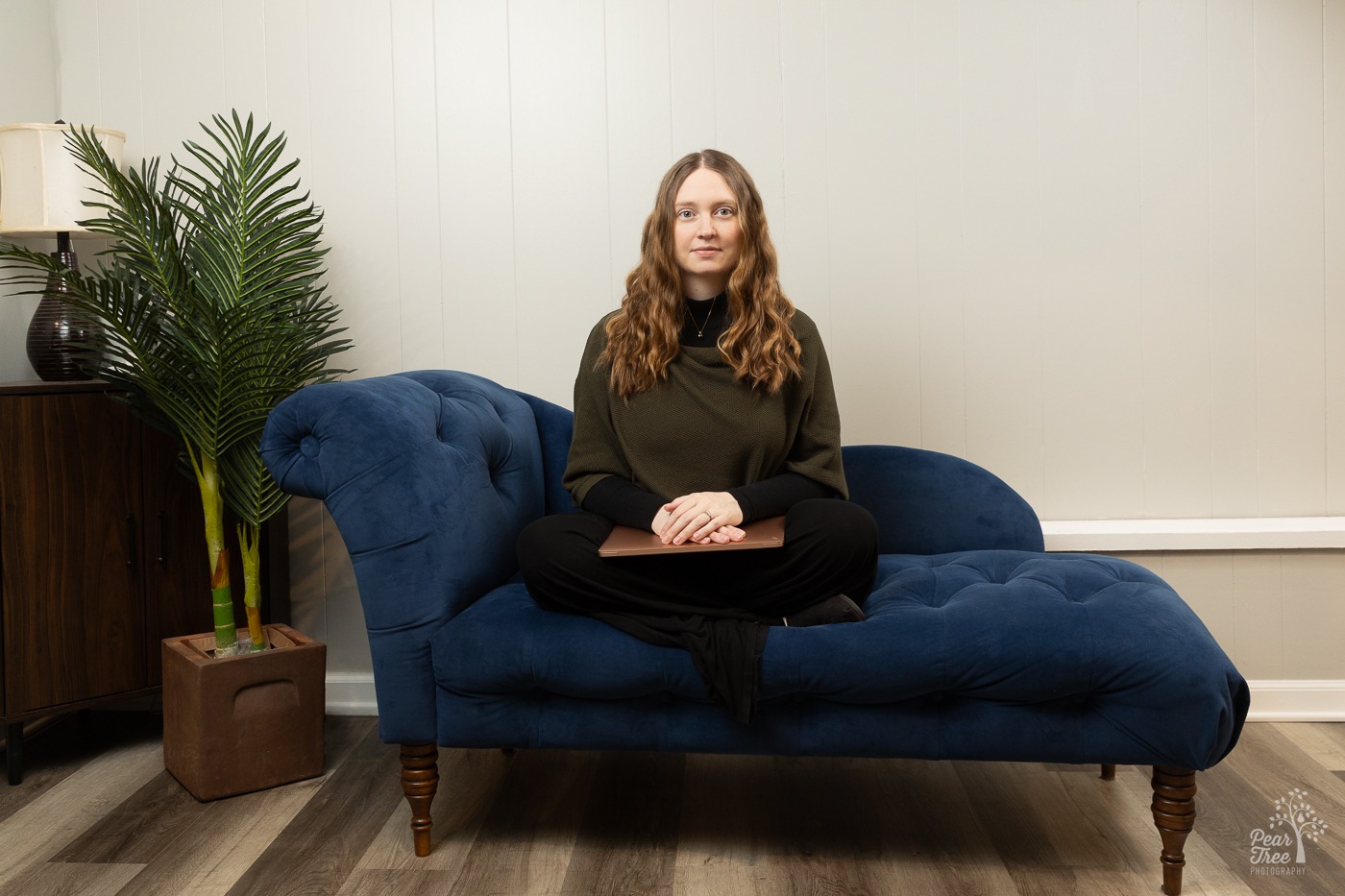 Dr. Hillary Langley sitting on a blue velvet chaise lounge next to a tall plant