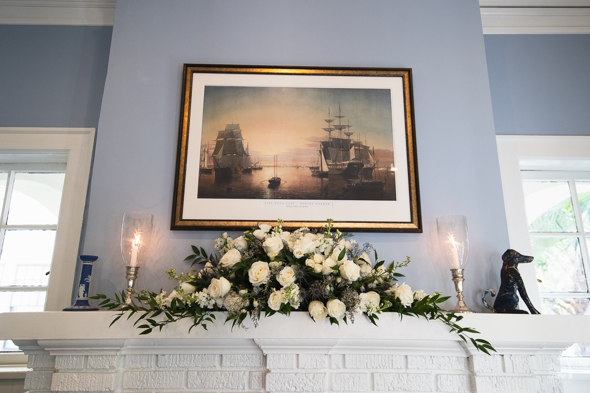 Framed painting hanging on a blue wall above white wedding flowers over a white brick fireplace