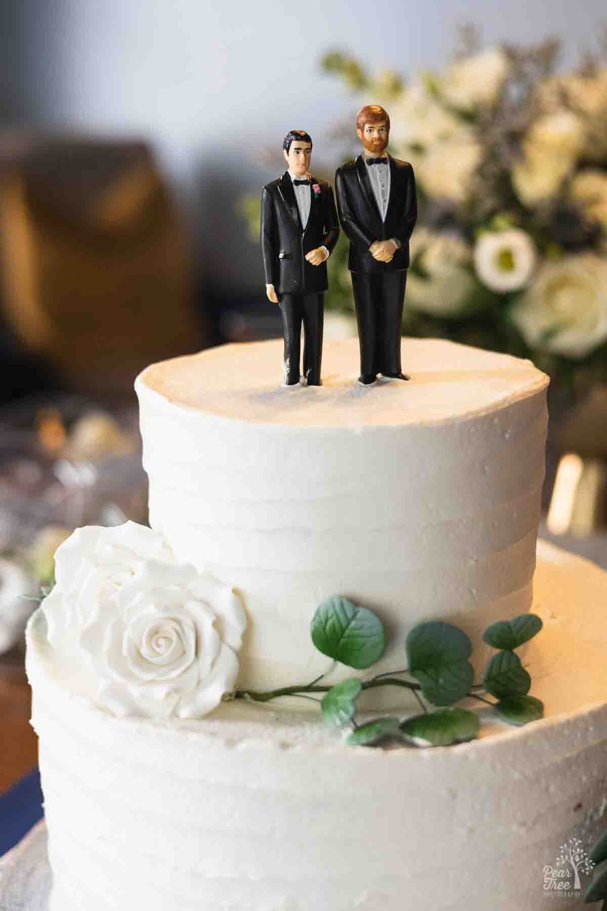 Two groom figurines standing on top of a beautiful white wedding cake