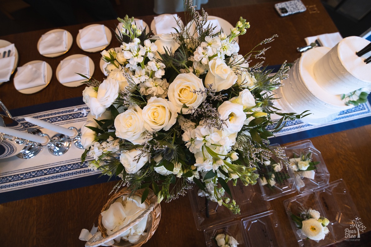 Overhead view of table bouquet of flowers next to a wedding cake, boutonnieres, and corsages