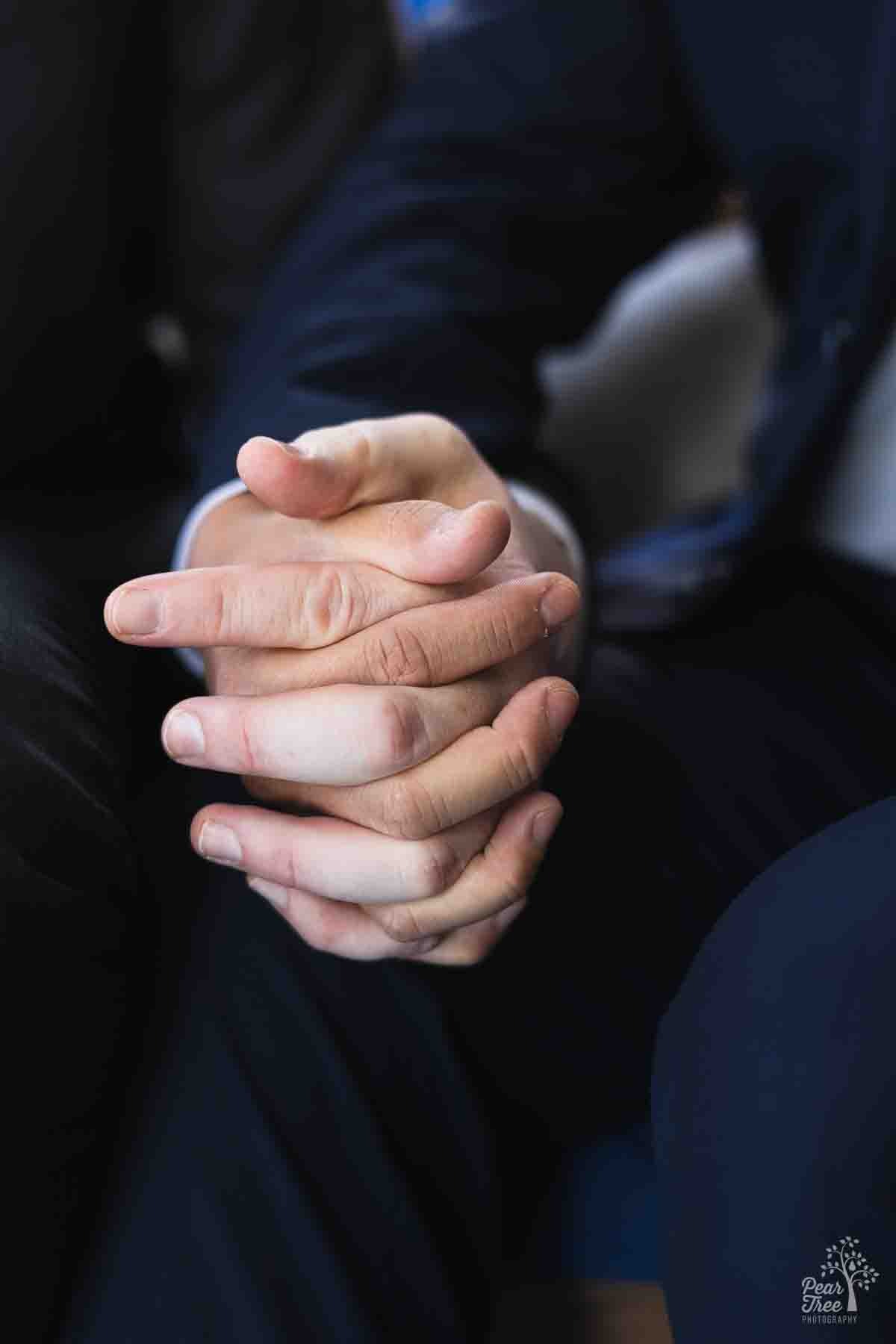 Waist view of two grooms sitting side by side and holding each other's hand