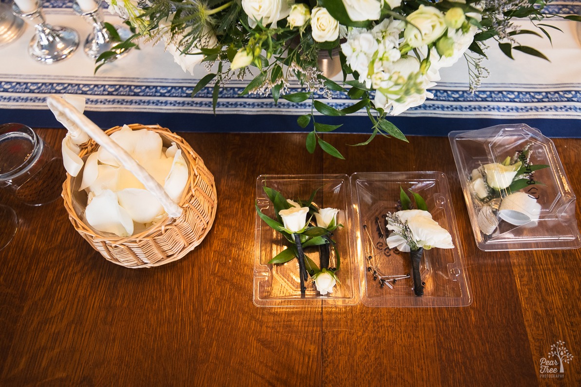 A basket of rose petals sitting on a table next to boutonieres for two grooms and two corsages for the mothers of the grooms