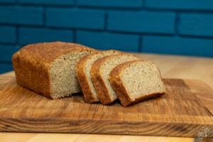 Neo Deli Nation gluten free bread loaf on a cutting board in front of a blue brick wall