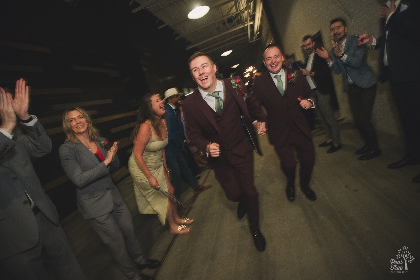 Running grooms laughing as friends and guests cheer and laugh with them