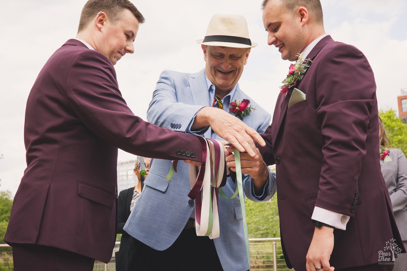 Happy family member tying a ribbon around the joined hands of two grooms