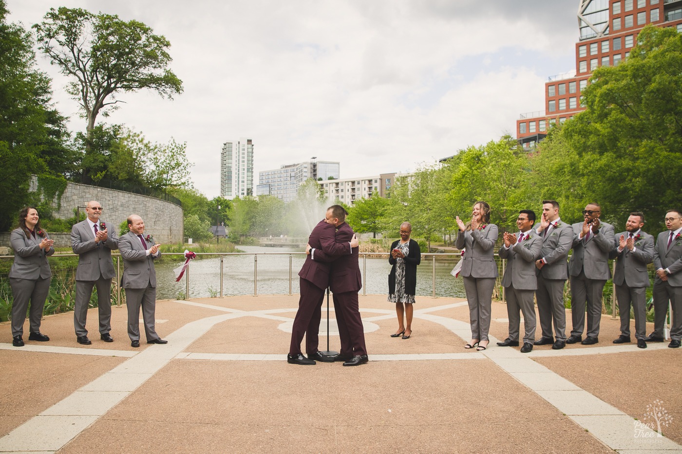 Two grooms in plum suits hugging while wedding party claps at Old 4th Ward wedding ceremony