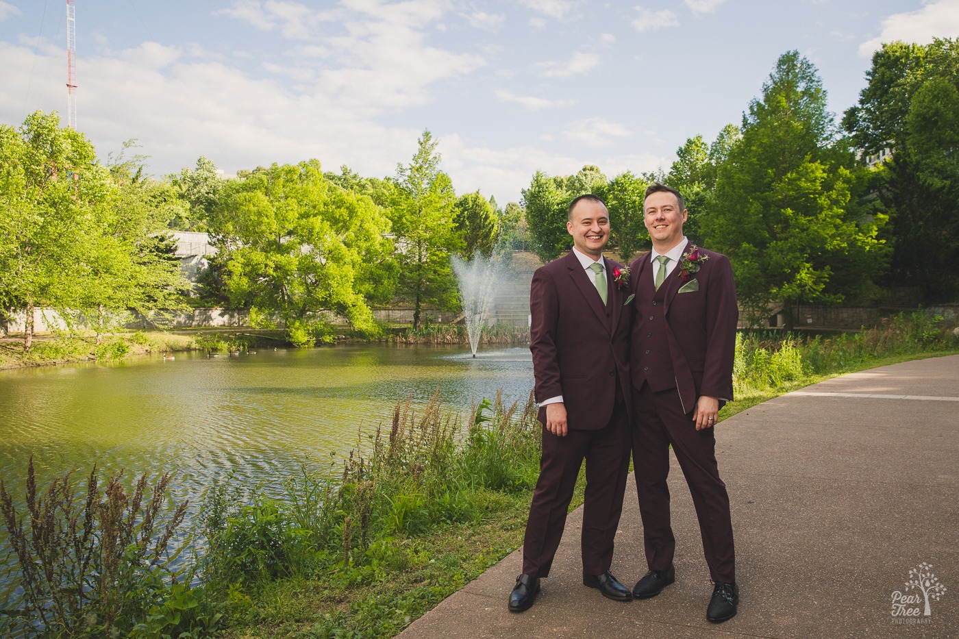 Two grooms smiling in plum suits with sage green ties at Old 4th Ward park