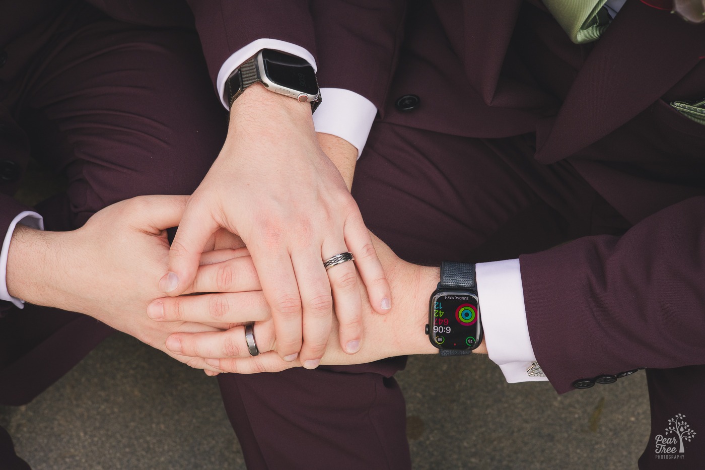 Hands, apple watches, and wedding bands of two grooms holding the other's hands