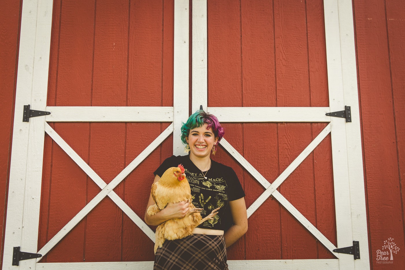 Smiling high school senior leaning against a red barn and holding a golden chicken