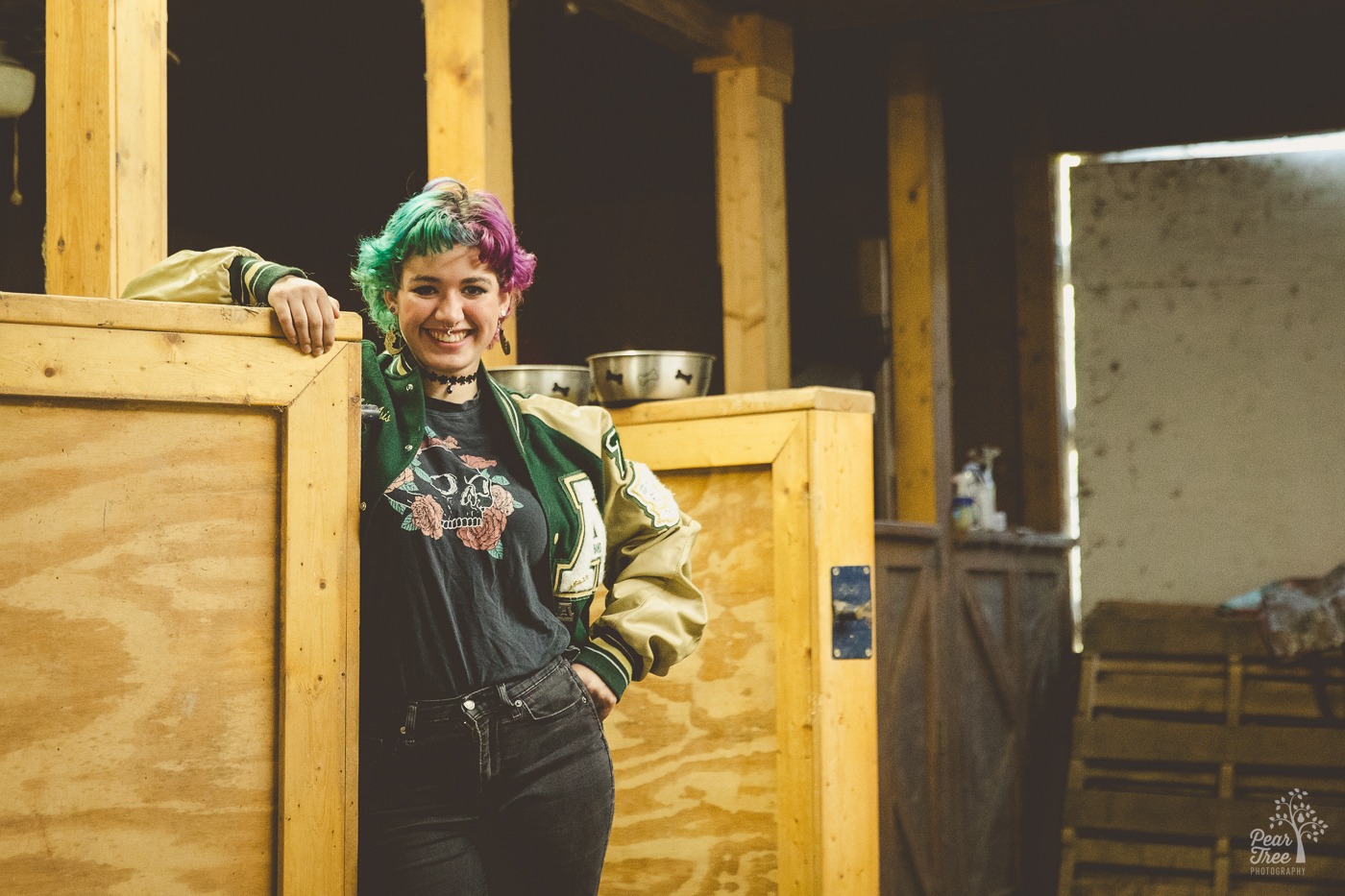 Happy Adairsville high school senior standing in an alpaca barn stall smiling while wearing jeans and her letterman jacket