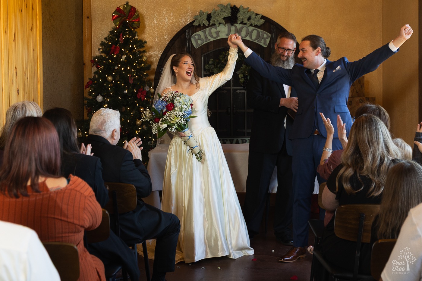 Bride with a humongous bouquet holding her new husband's hand up in the air in front of Big Door Vineyard sign