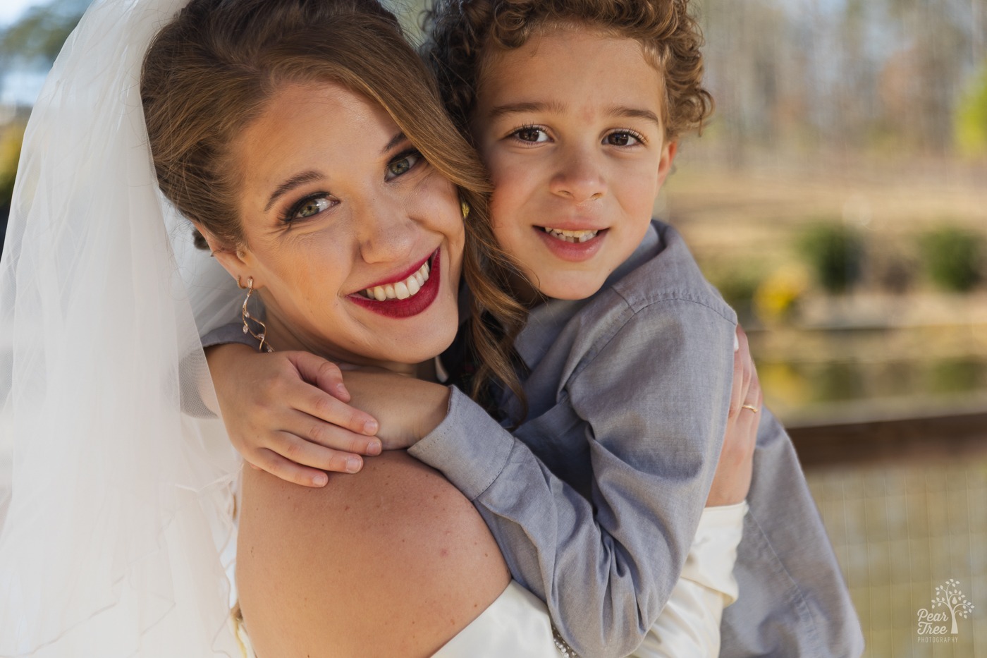 Gorgeous smiling bride with bright red lips holding her little boy close in a hug
