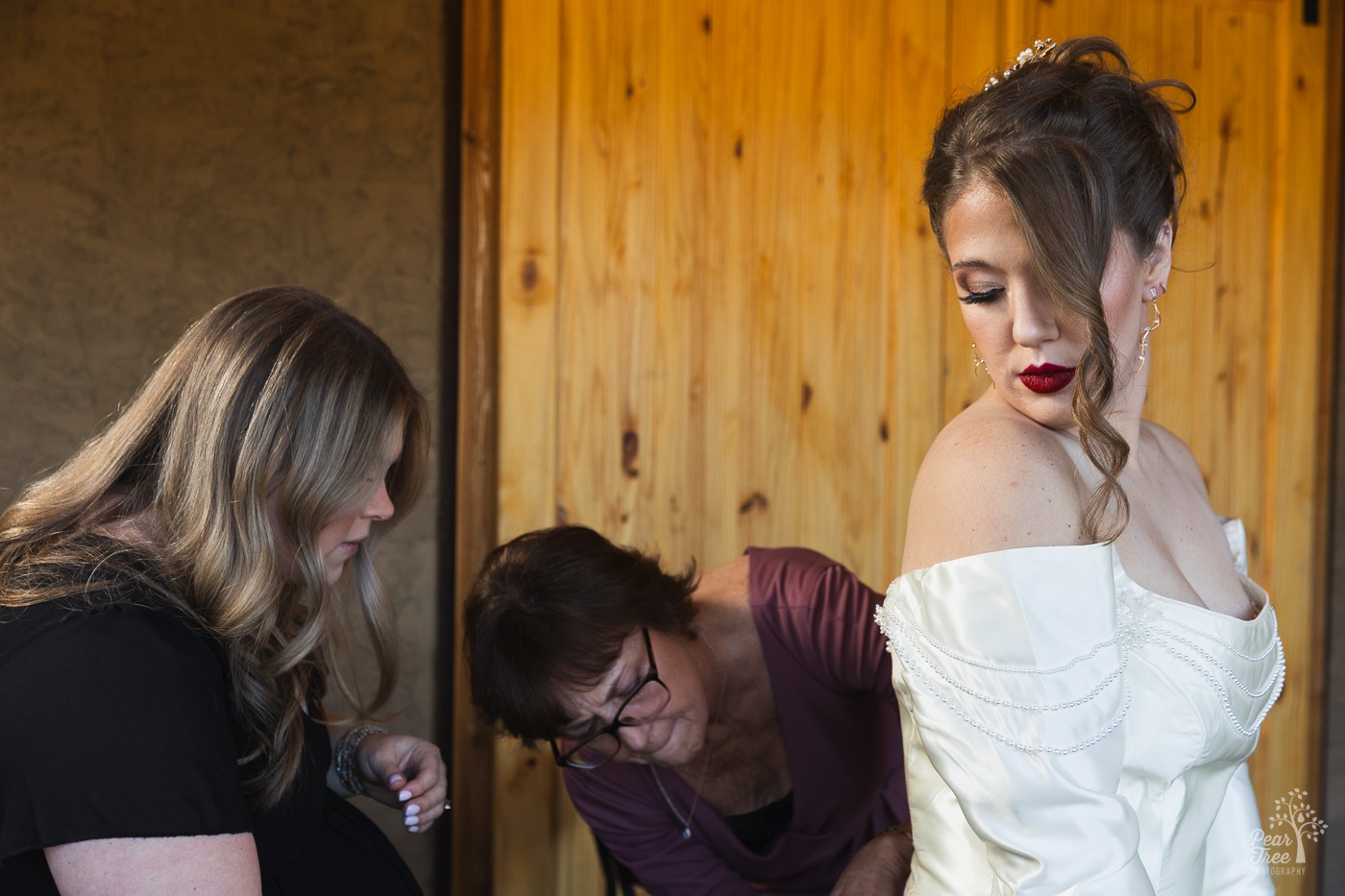 Bride looking back over her shoulder as a friend and mom button up the back of her wedding dress