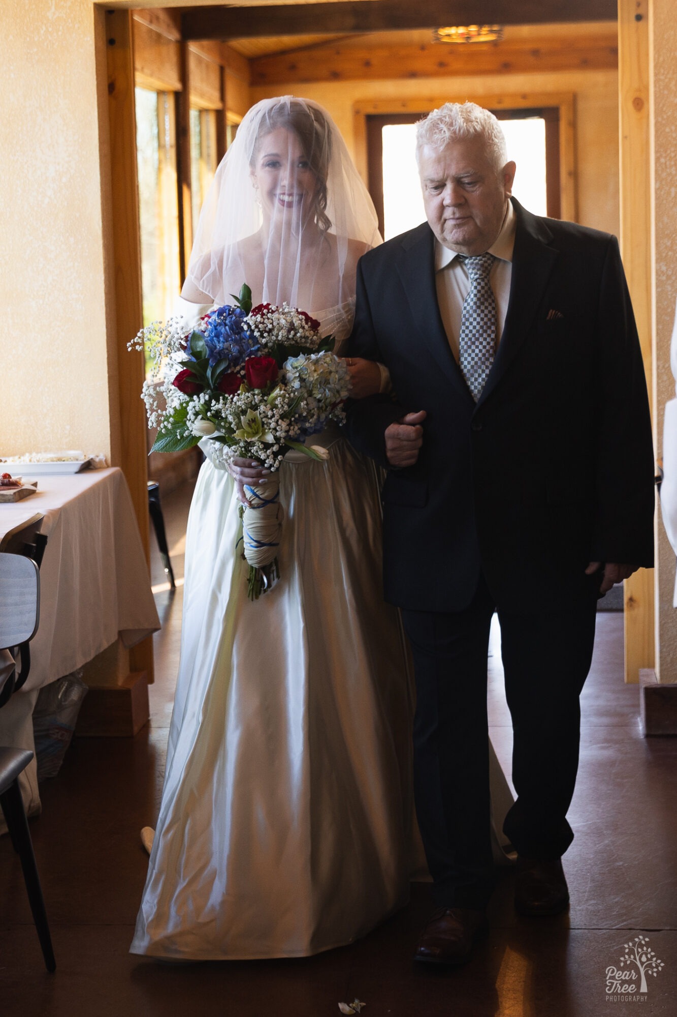 Father walking his daughter bride down the aisle at a Big Door vineyard wedding. Her face is covered with a veil and she is holding a humongous bouquet of flowers