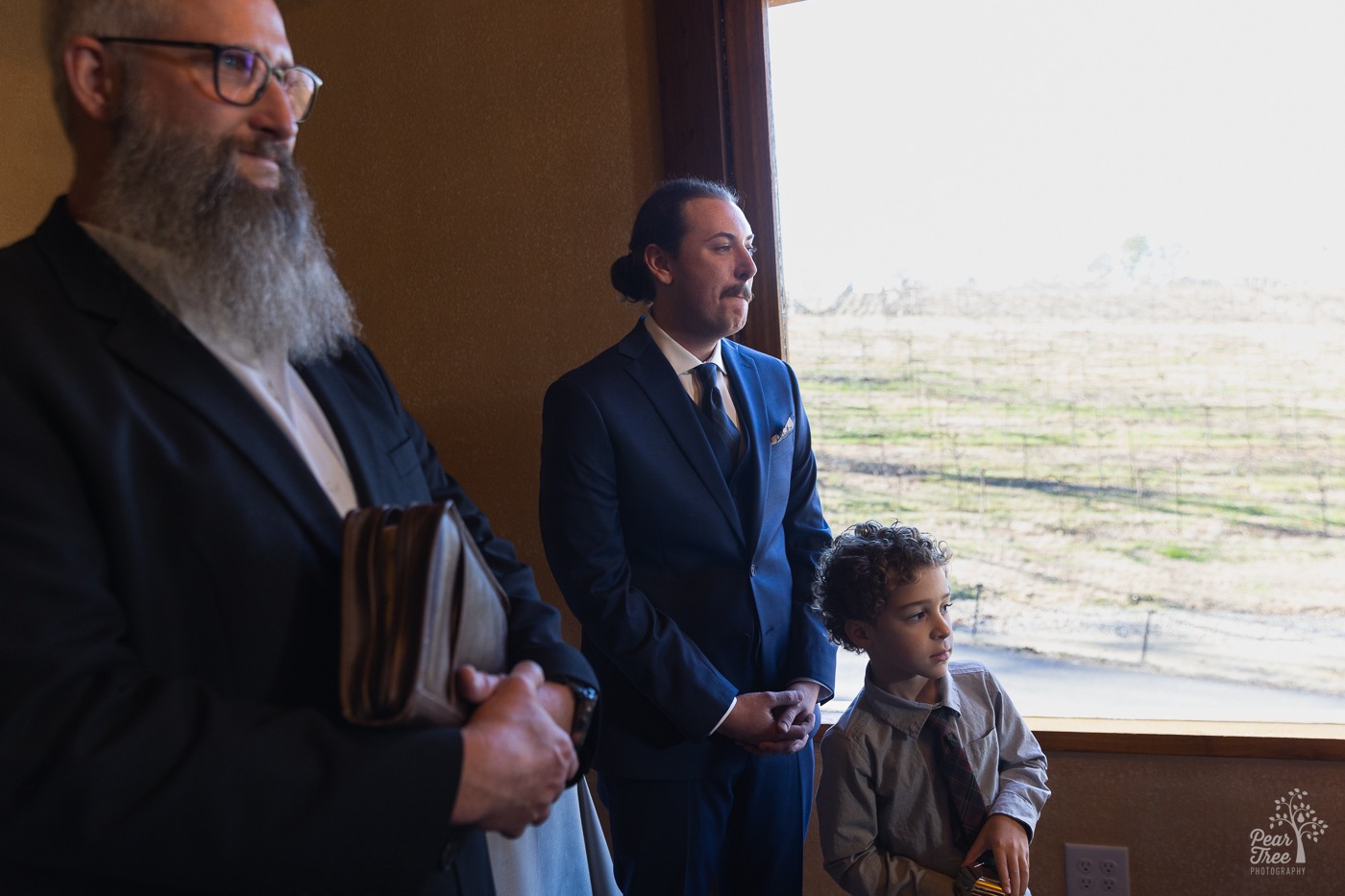 Groom and bride's son watching her walk down the aisle with a vineyard in the background through the window