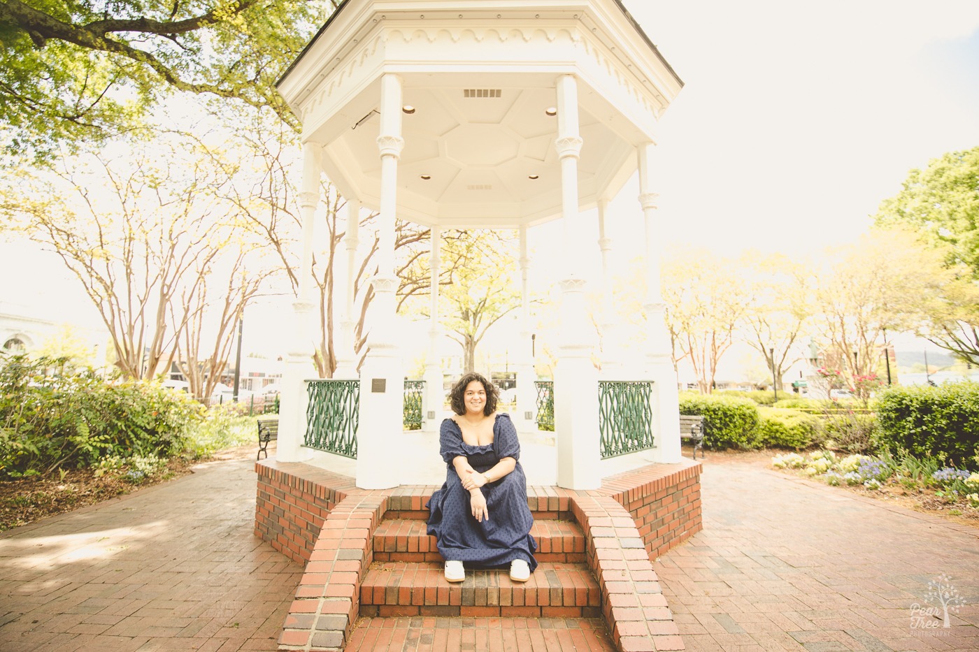 Teenage girl sitting on gazebo steps in a blue dress and smiling at the camera