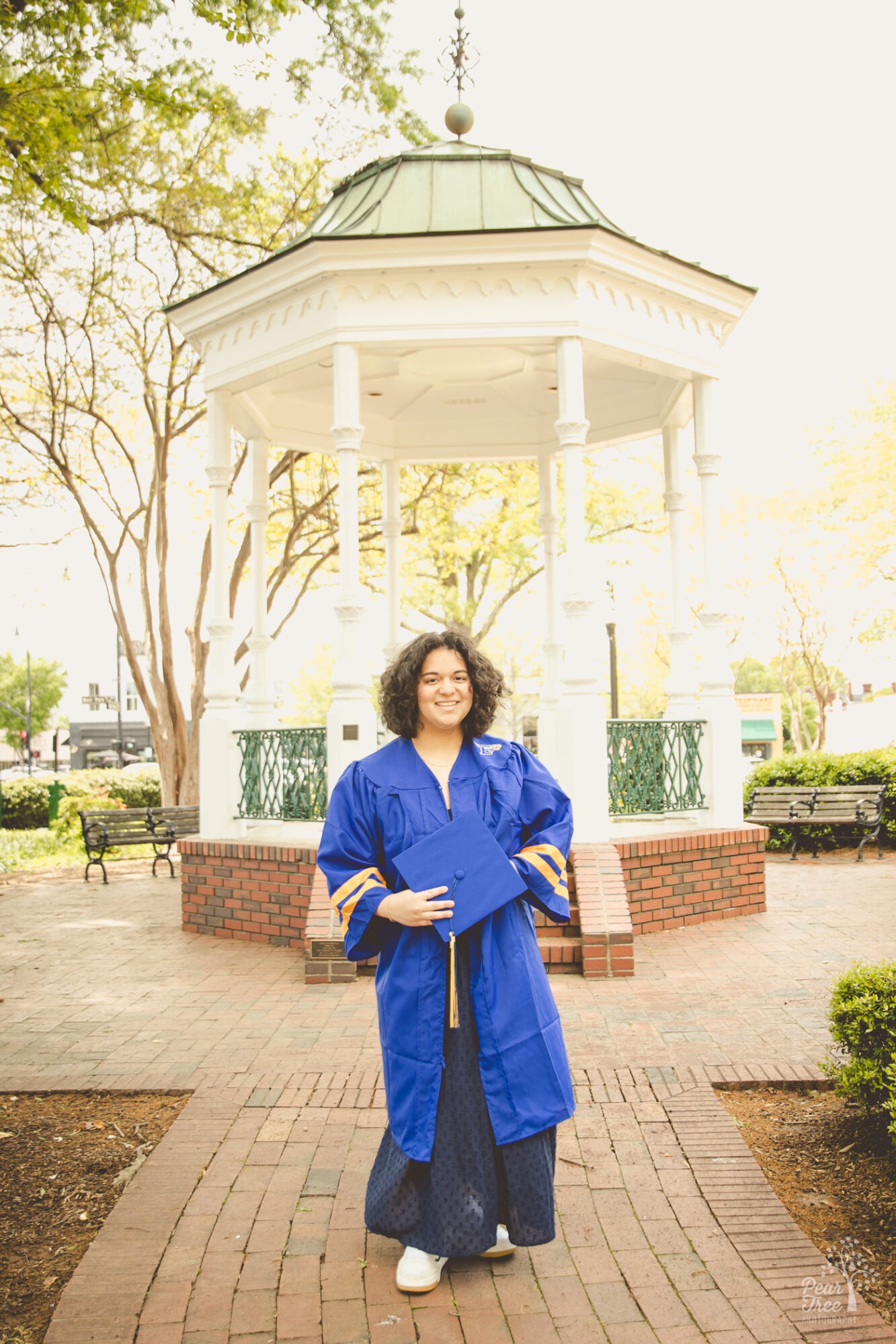 High school senior girl in cap and gown in front of a white gazebo