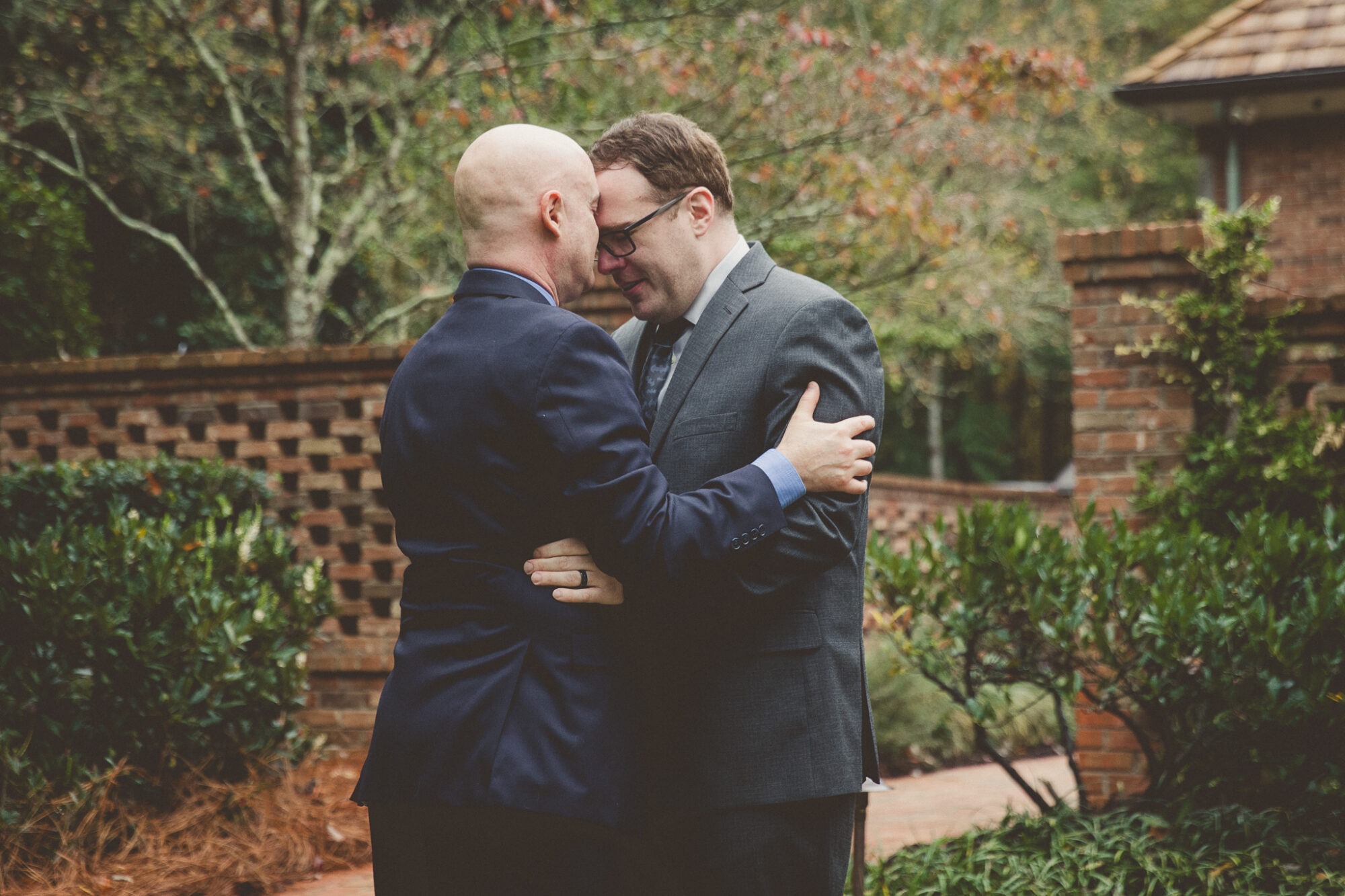 Two grooms in suits holding each other close, touching foreheads after being married in a backyard Atlanta wedding ceremony