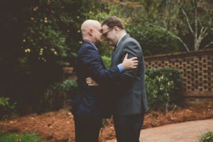 Two grooms grounding each other in a close hug and touching foreheads after their backyard Atlanta wedding ceremony
