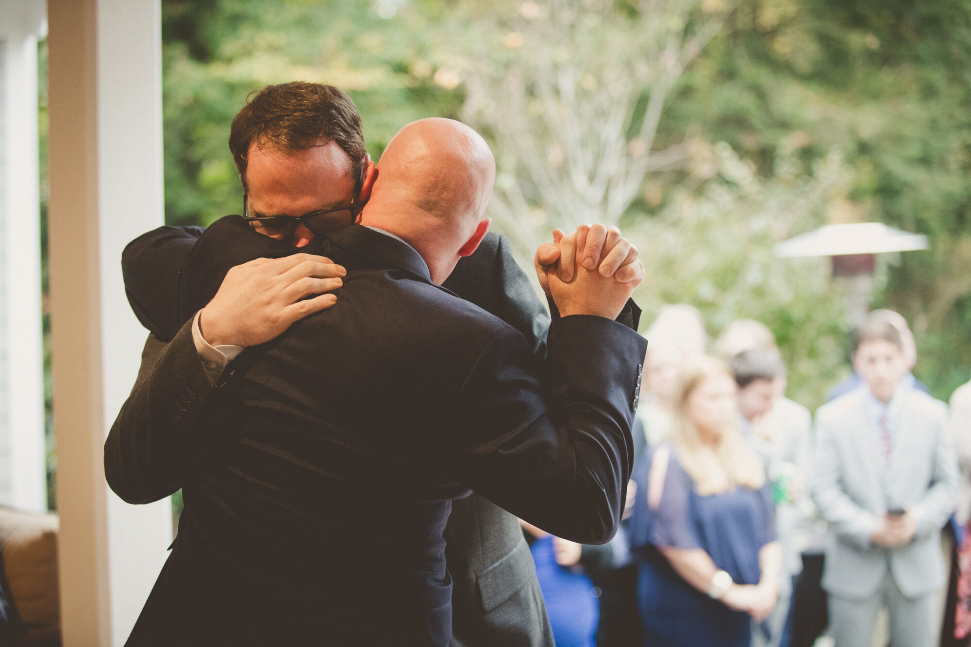 Two grooms burying their faces in each other's shoulders in the middle of their first dance after their backyard Atlanta wedding ceremony