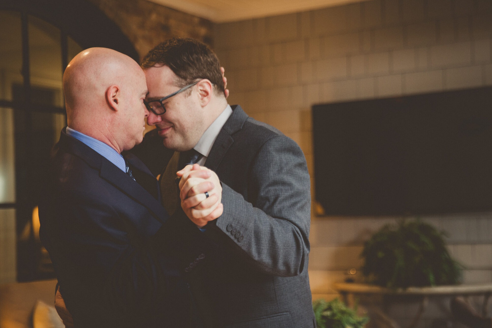 Two grooms in their first dance after the wedding with foreheads touching and one holding the back of the other's head