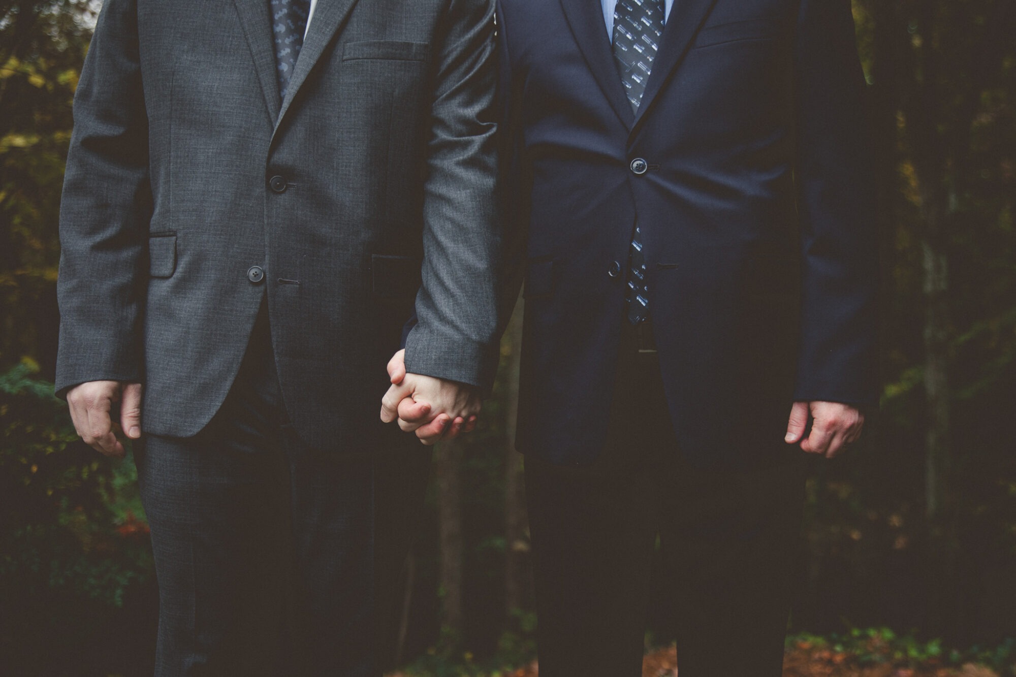 Chest to knees view of two grooms wearing suits with a Batman and Star Wars ties while holding hands before their backyard Atlanta wedding ceremony