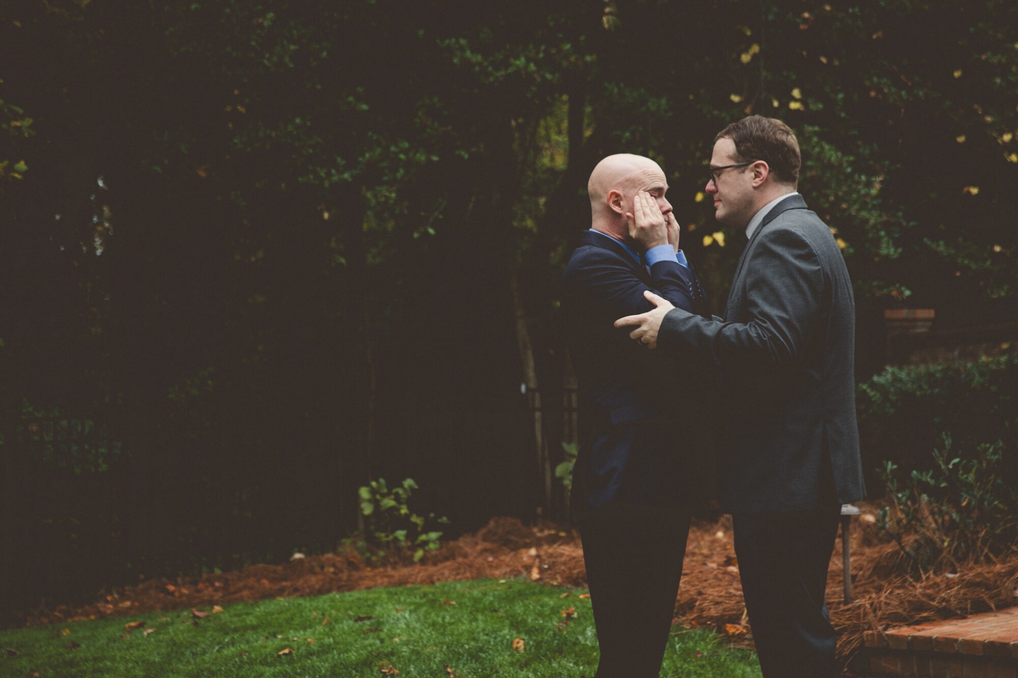 One groom holding his husband's arms while the other groom wipes tears away from his eyes