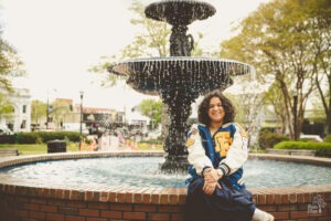 Etowah High School senior sitting in front of Marietta Square fountain smiling and wearing her letterman jacket