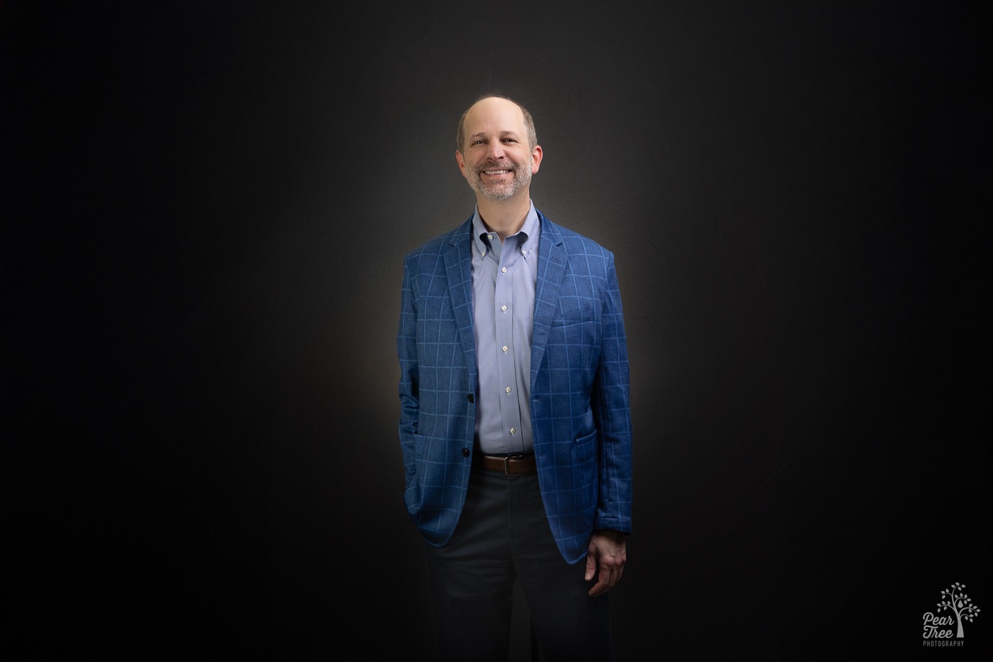 National business coach Joe Woodard wearing a blue blazer and shirt in front of a dark background