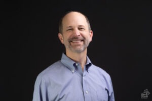 National business coach headshot of Joe Woodard in a blue shirt and dark background