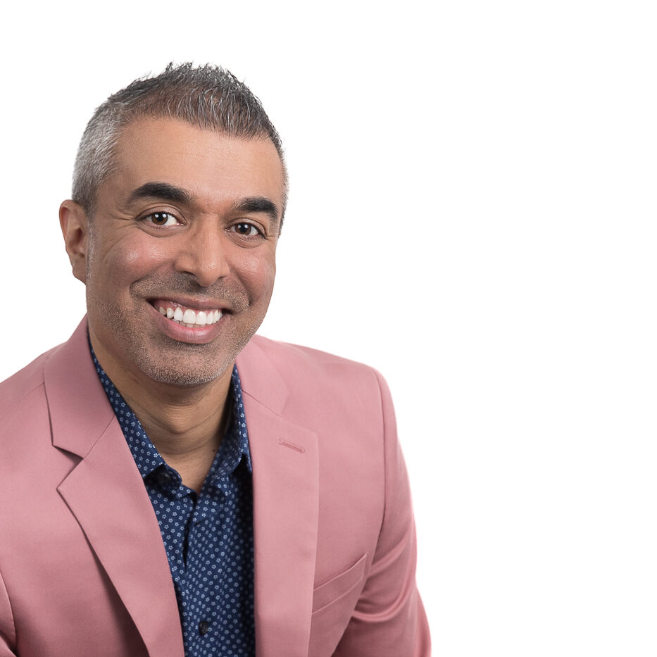 Professional headshot of Minesh Patel, Realtor. He's wearing a mauve blazer, patterned blue button down, and a big smile.