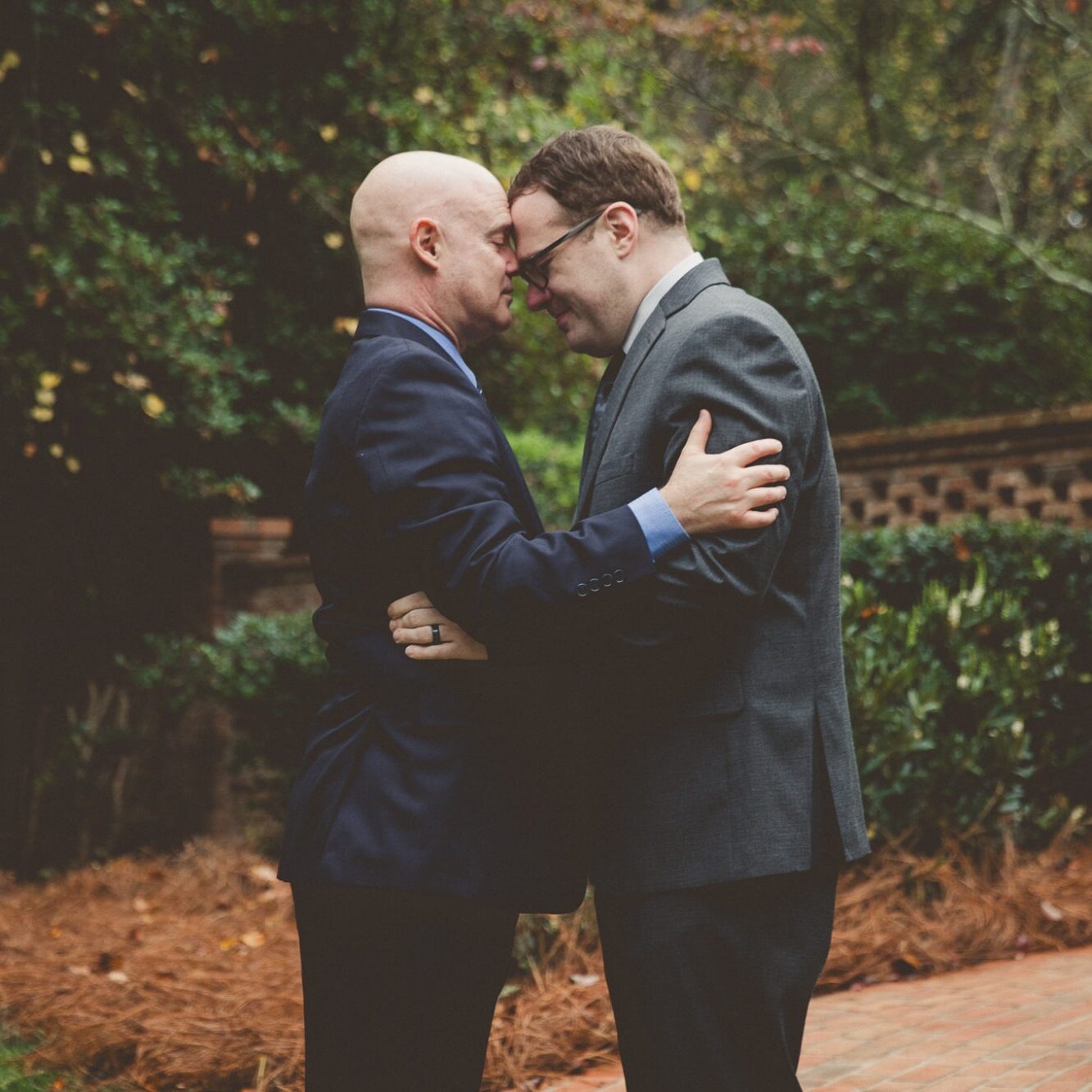 Two grooms grounding each other in a close hug and touching foreheads after their backyard Atlanta wedding ceremony