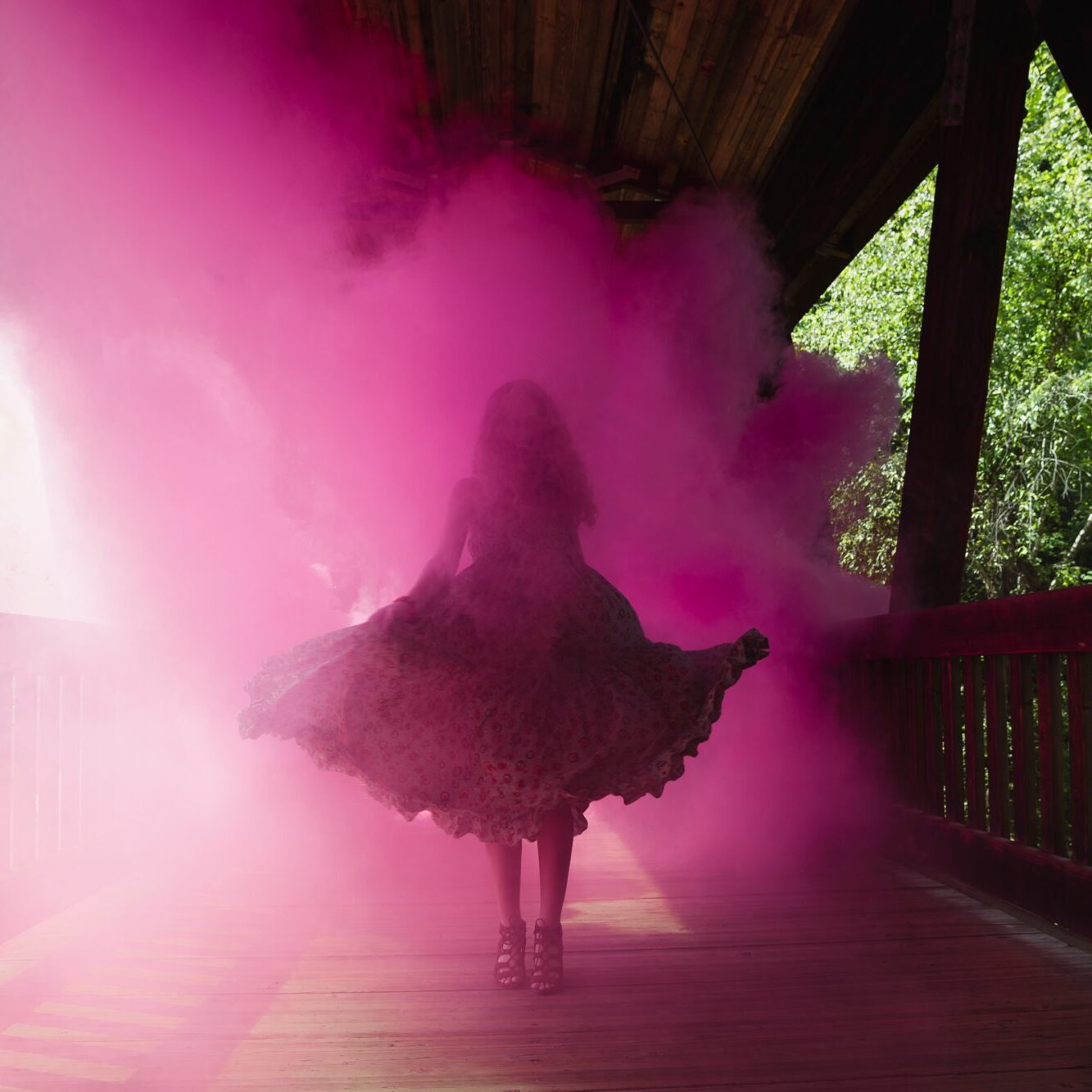 High school senior twirling in pink smoke on a covered bridge