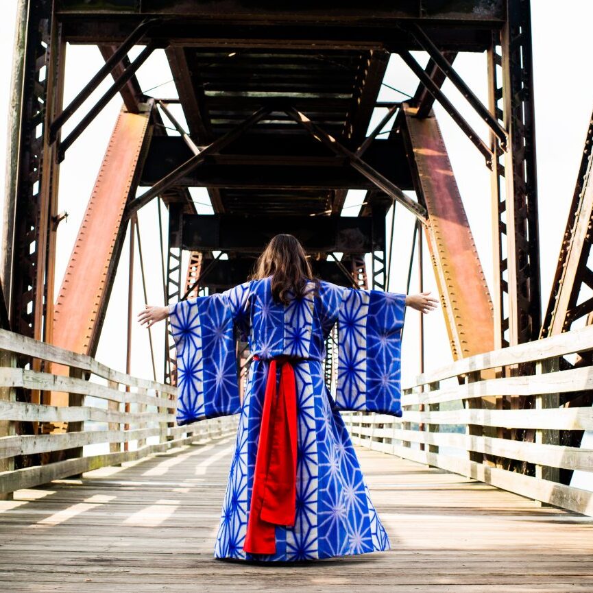 High school senior wearing purple and red kimono with arms outstretched in the middle of a bridge
