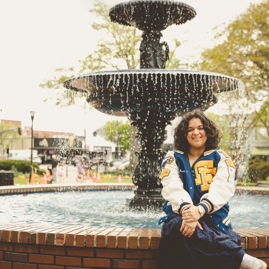 Etowah High School senior sitting in front of Marietta Square fountain smiling and wearing her letterman jacket