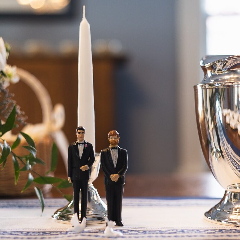 Two groom figurines standing on a table top in front of a candle and with small white doves prior to being placed on top of a wedding cake for an intimate wedding in Midtown Atlanta