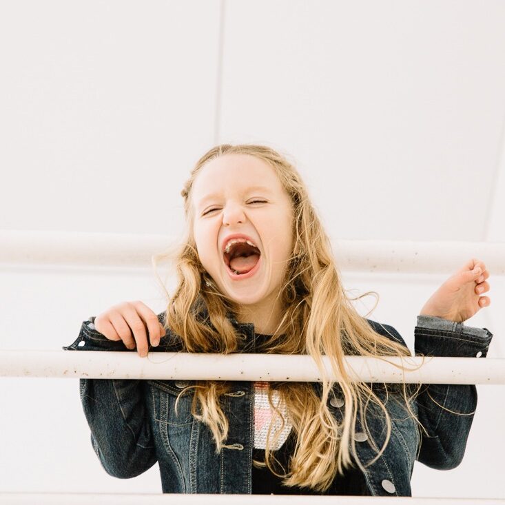 Little girl laughing with long blond hair and toothless smile