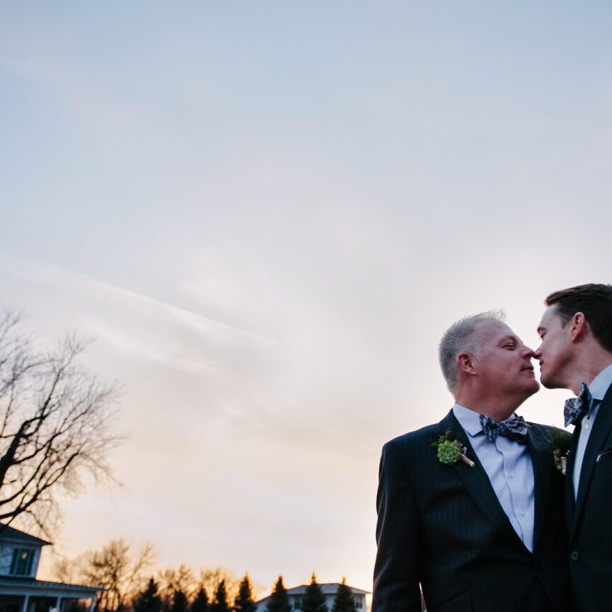 Two grooms almost kissing at sunset