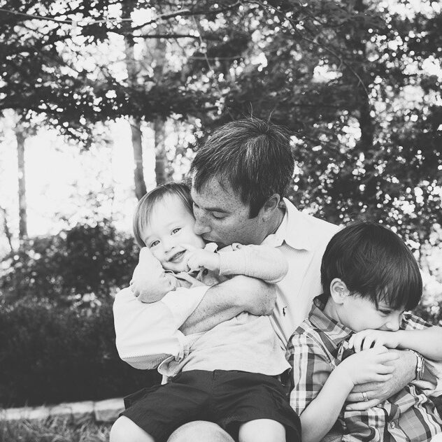 A dad holding his two little boys tight and smooching one on the cheek