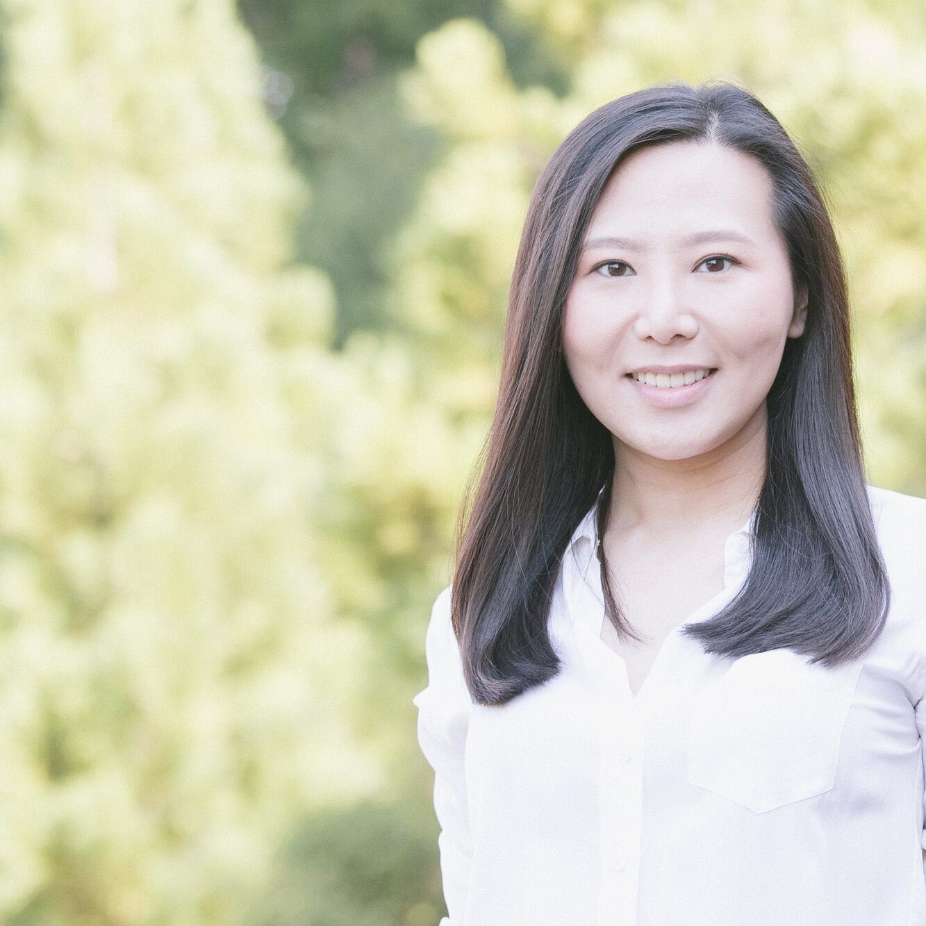 Smiling Chinese woman standing in front of out-of-focus trees