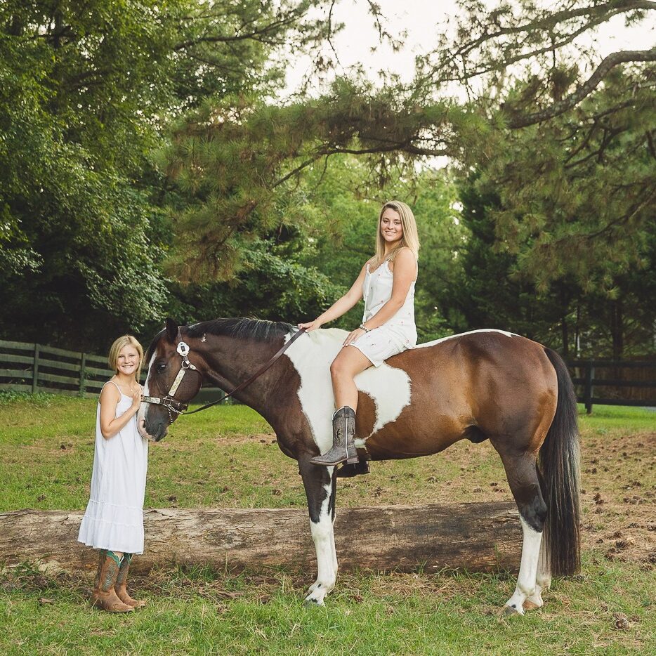 Two sisters in white sundresses and cowgirl boots in a Woodstock field with their paint horse