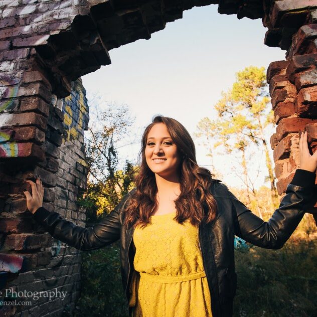 High school senior girl in yellow dress and black leather jacket standing in open brick doorway at Mason Mill Park
